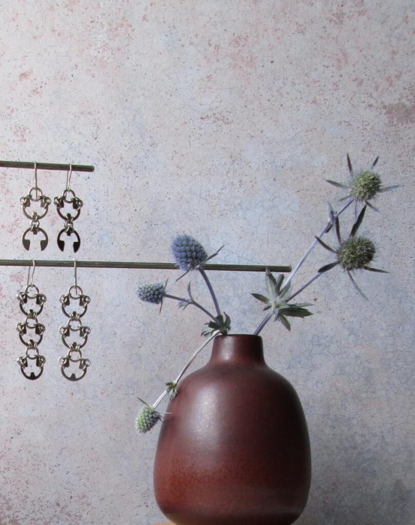 Blue sea holly flowers in a small modern bud vase, with Wraptillion's Scarab Earrings and Lotus Earrings.