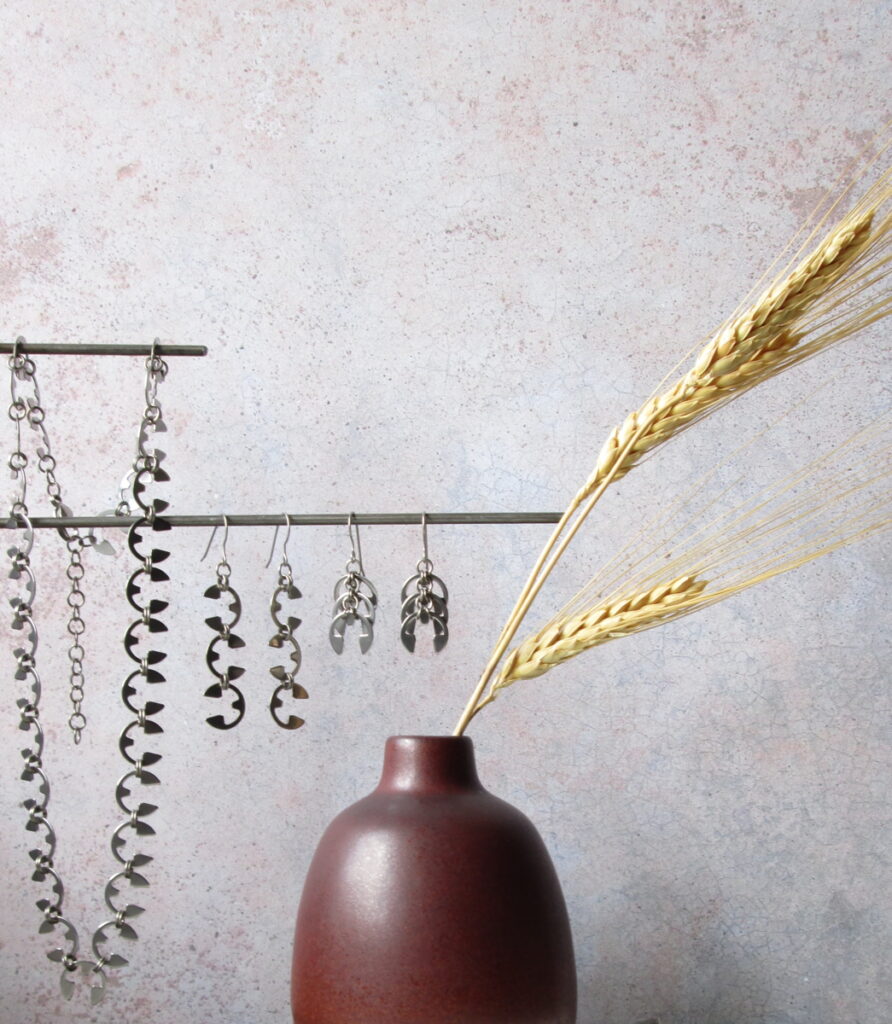 Dried wheat in a small modern bud vase, displayed with the Fern Necklace, Vine Earrings, and Fir Cone Earrings in Wraptillion's studio.