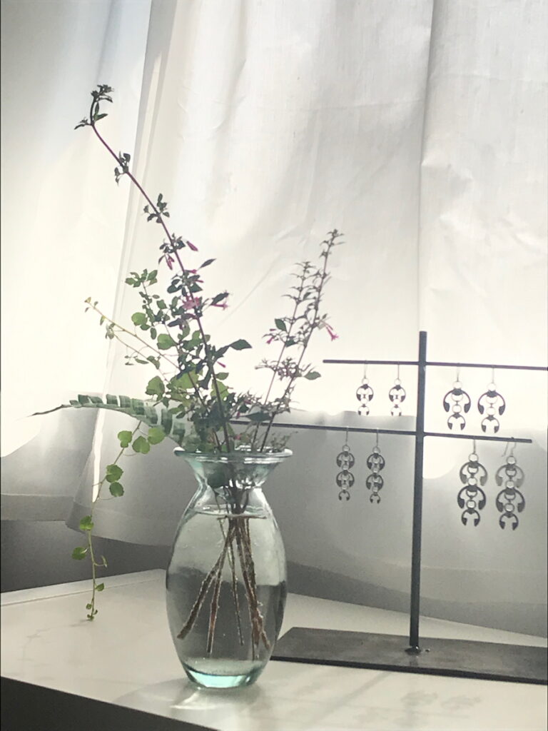 Fuchsia 'Isis' and procumbens cuttings with a fern frond in a vase in Wraptillion's studio, with the Hops Earrings, Short Fuchsia Earrings, Long Fuchsia Earrings, and Laburnum Earrings.