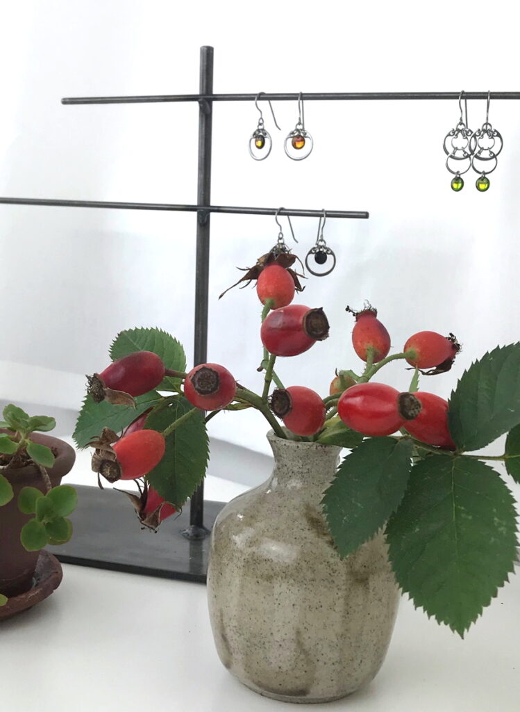 Rosa alba hips and a small potted sedum on Wraptillion's desk, with earrings from the Industrial Glass collection.