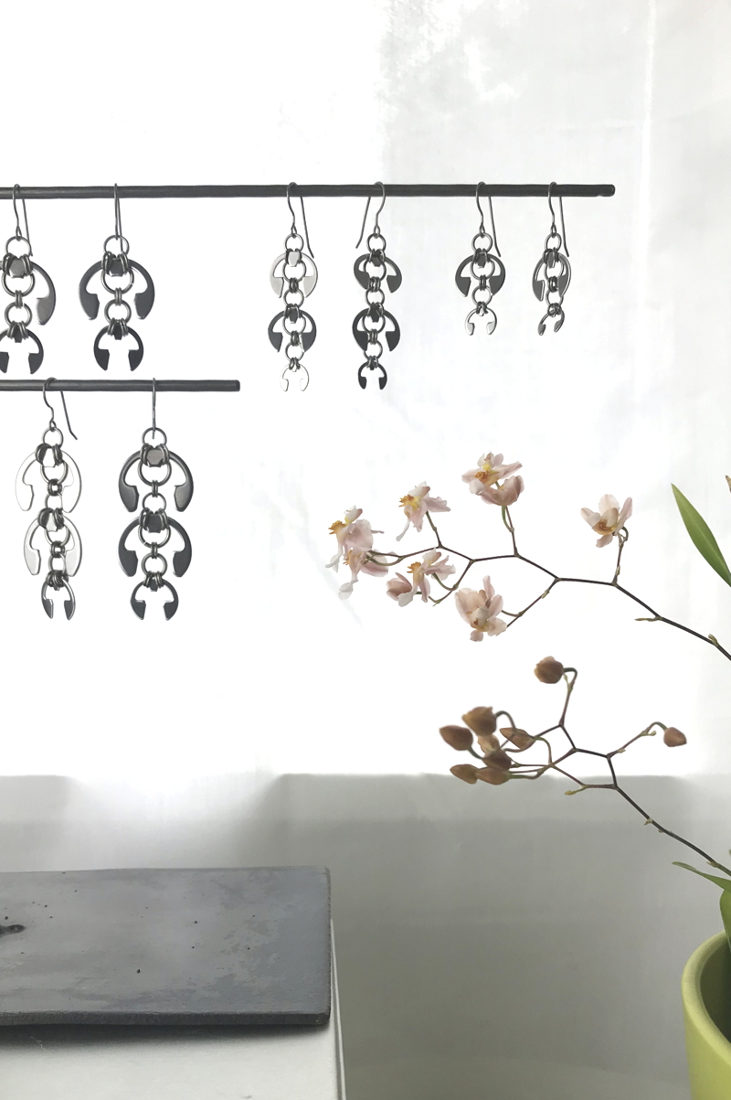 Wraptillion's Hops Earrings, Laburnum Earrings, Long Fuchsia Earrings, and Short Fuchsia Earrings, on a jewelry stand with orchid Oncidium 'Tsiku Marguerite' in a studio.