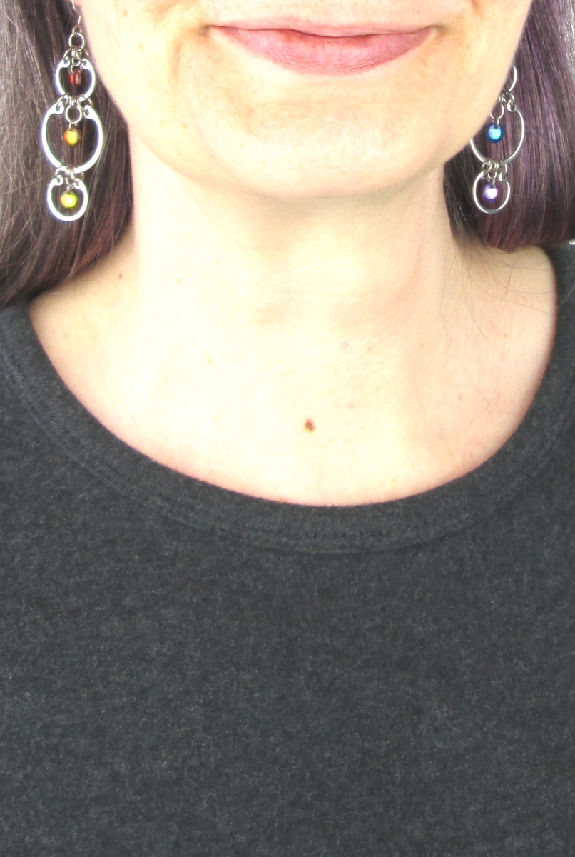 Close cropped modeled photo of Wraptillion's Alternating Rainbow Earrings with a dark gray top