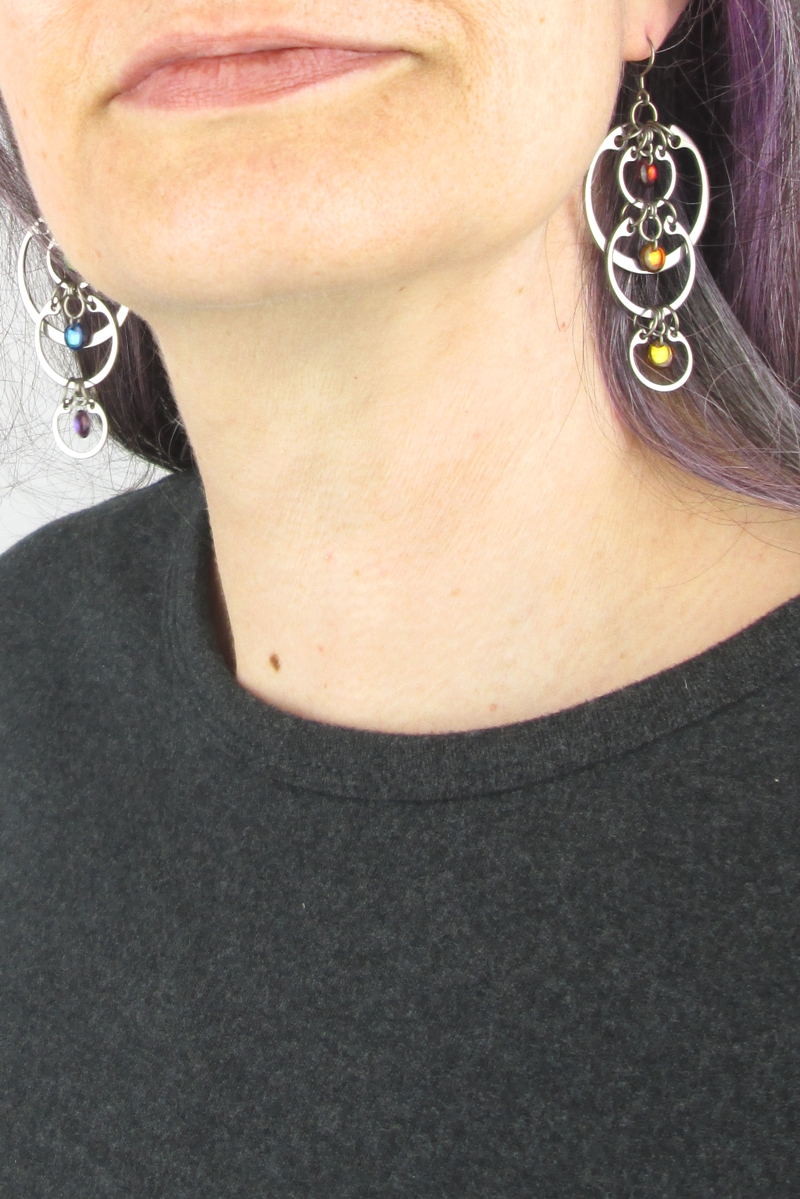 Cropped photo of artist Kelly Jones wearing Wraptillion's modern linked circle Cascading Rainbow Earrings with a dark gray top.