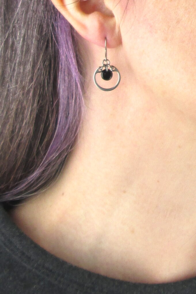 closeup photo of one of Wraptillion's small modern silver-tone circle earrings in black modeled