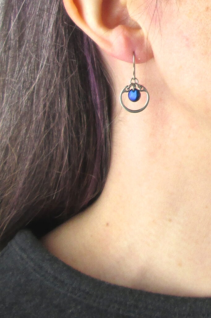 closeup photo of one of Wraptillion's small modern silver-tone circle earrings in navy blue modeled