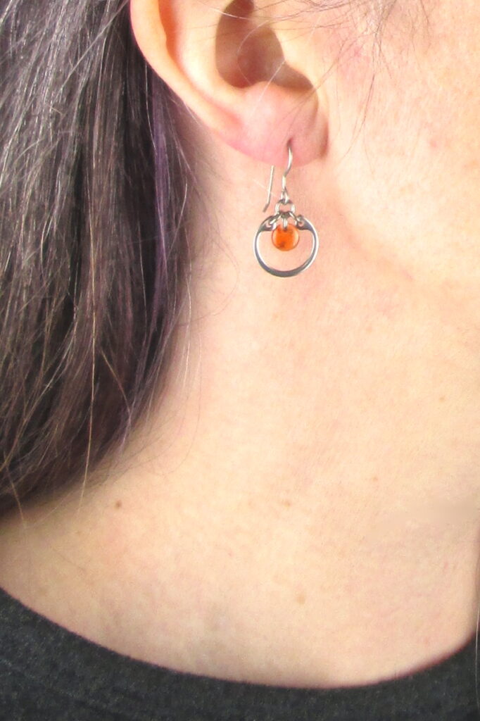 closeup photo of one of Wraptillion's small modern silver-tone circle earrings in orange modeled