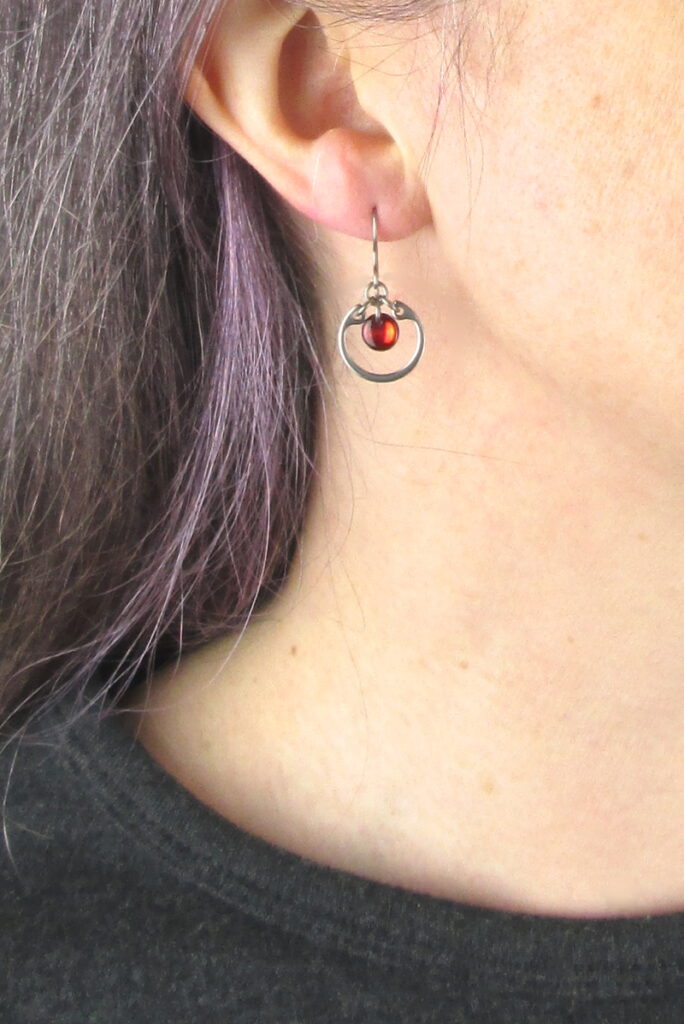 closeup photo of one of Wraptillion's small modern silver-tone circle earrings in red modeled