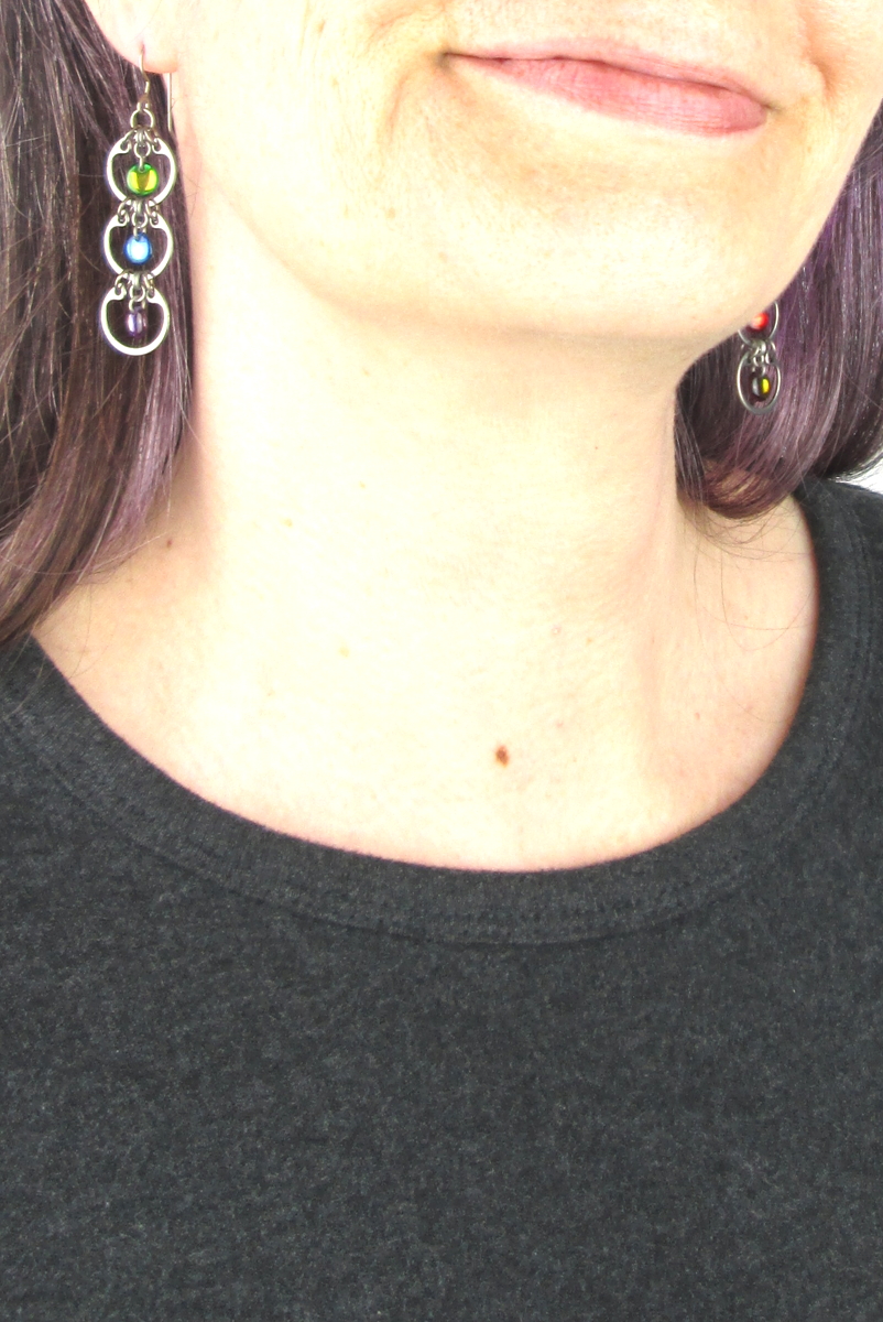 Close cropped modeled photo of Wraptillion's Tripled Rainbow Earrings with a dark gray top