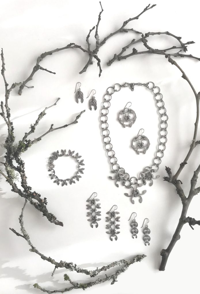 Closeup of botanical-inspired jewelry from Wraptillion's Mechanical Garden collection, surrounded by bare plum branches in winter.