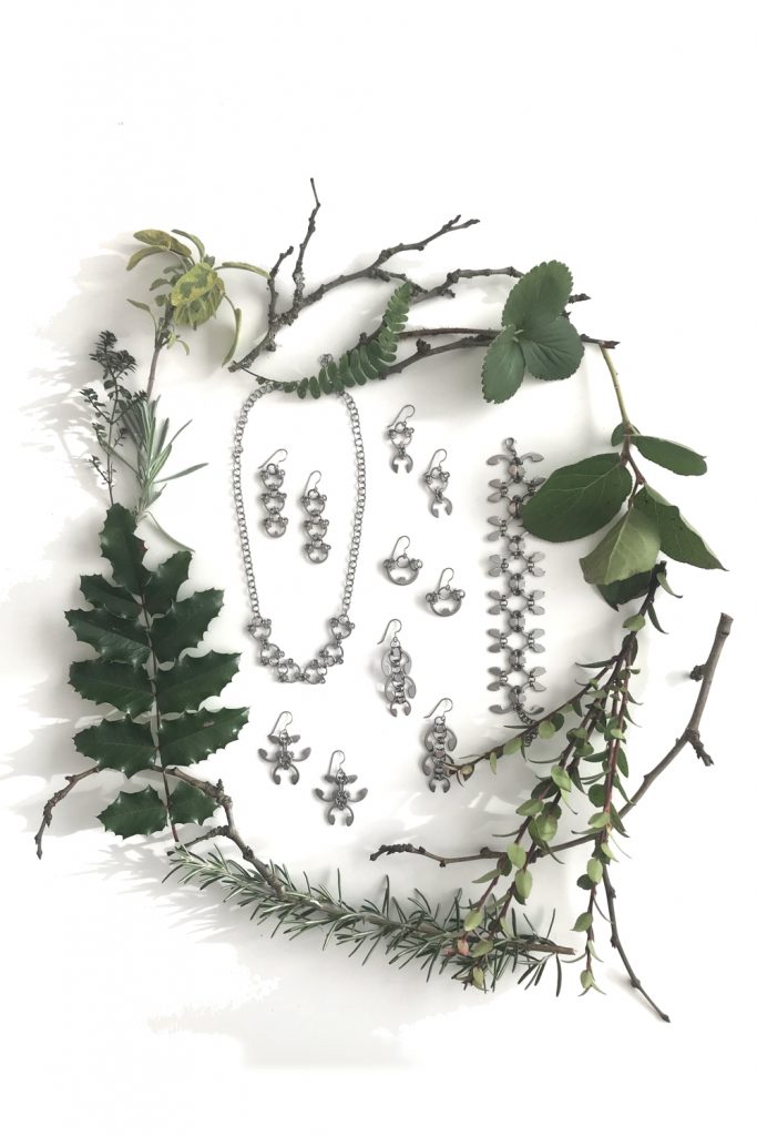 Botanical-inspired jewelry from Wraptillion's Mechanical Garden collection, surrounded by branches from plum, mahonia, salal, rosemary, and other evergreen plants.in winter.