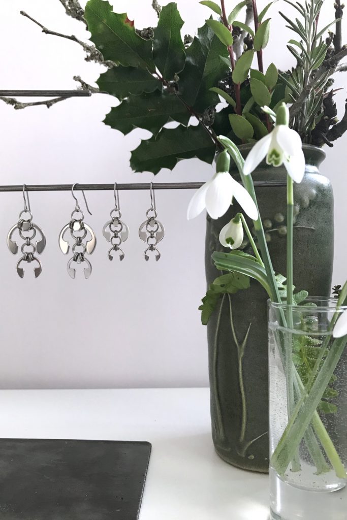 cut snowdrops in a small glass vase with a fern frond, shown in front of another small winter floral arrangement and Wraptillion's Hops Earrings and Short Fuchsia Earrings