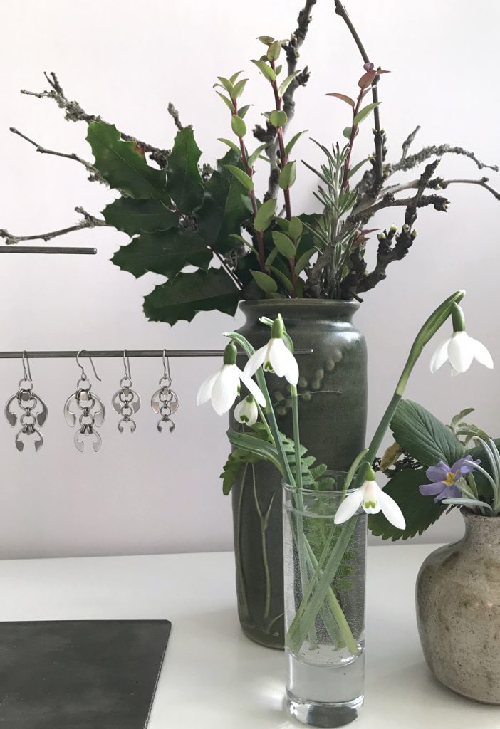 cut snowdrops in a small glass vase with a fern frond, shown in front of other small winter flower arrangements and Wraptillion's Hops Earrings and Short Fuchsia Earrings