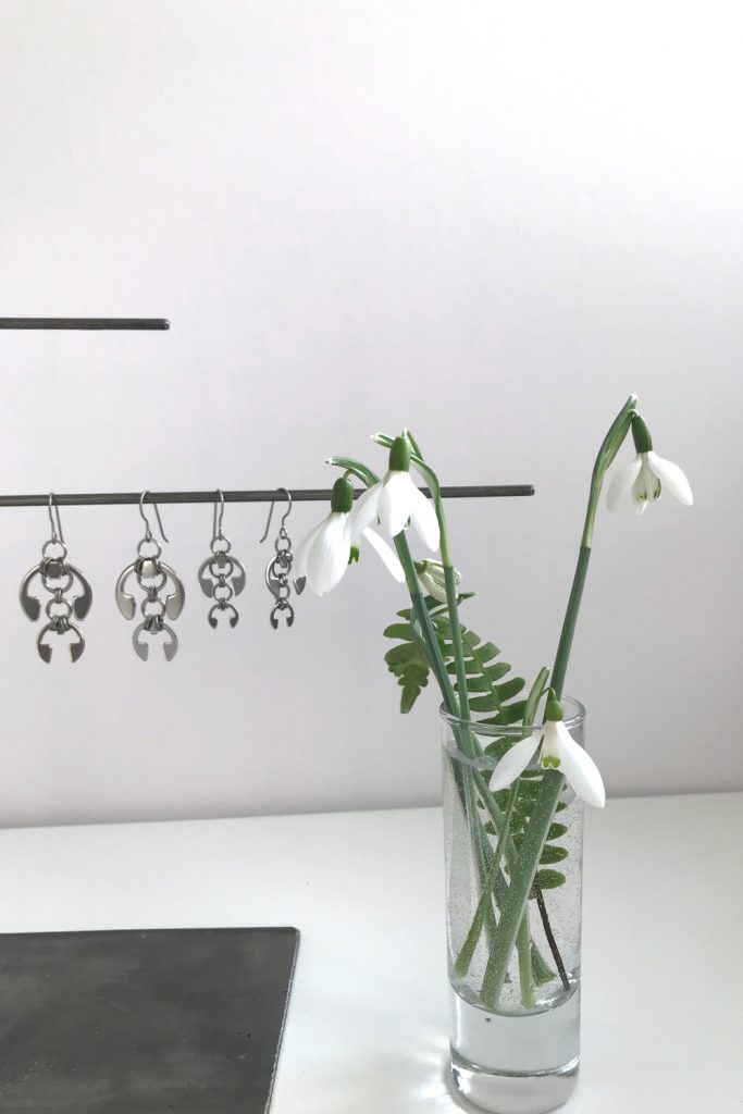 cut snowdrops in a small glass vase with a fern frond, shown in front of Wraptillion's Hops Earrings and Short Fuchsia Earrings