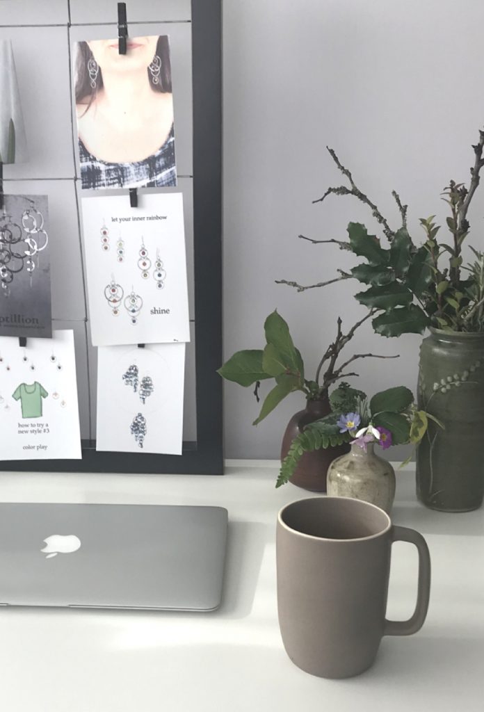 A glimpse into Wraptillion's studio workspace: laptop, mug, three small everyday winter flower arrangements, and the corner of a moodboard.