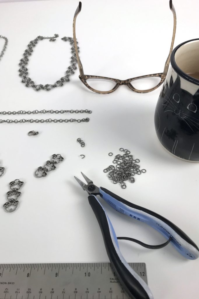 Kelly Jones of Wraptillion's studio workspace, with the Delicate Lotus Necklace in progress, shown with pliers, reading glasses, and a mug of tea.