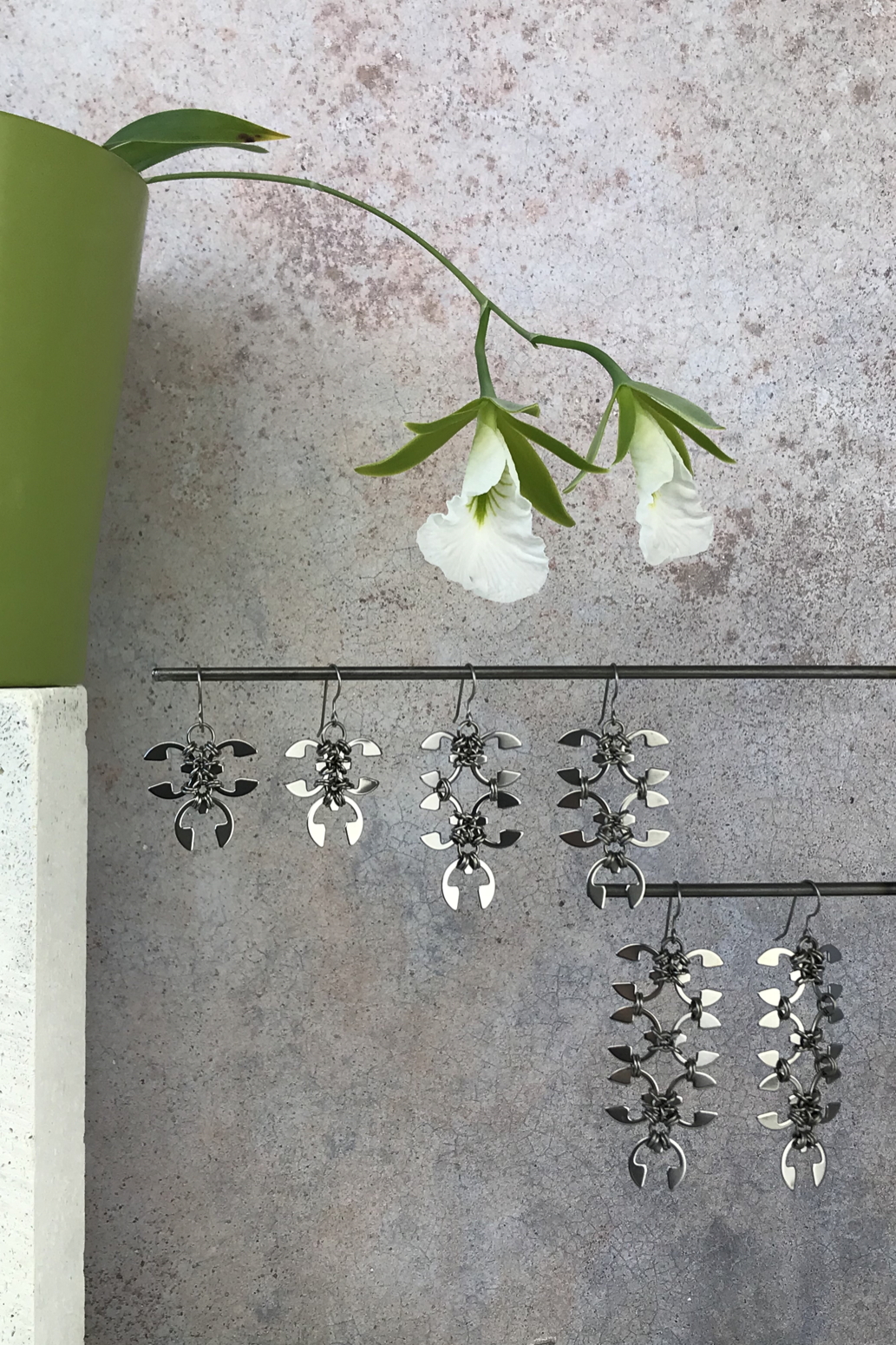 Wraptillion's Ivy Earrings, Short Wisteria Earrings, and Long Wisteria Earrings with blooming Encyclia mariae in front of a textured gray wall.