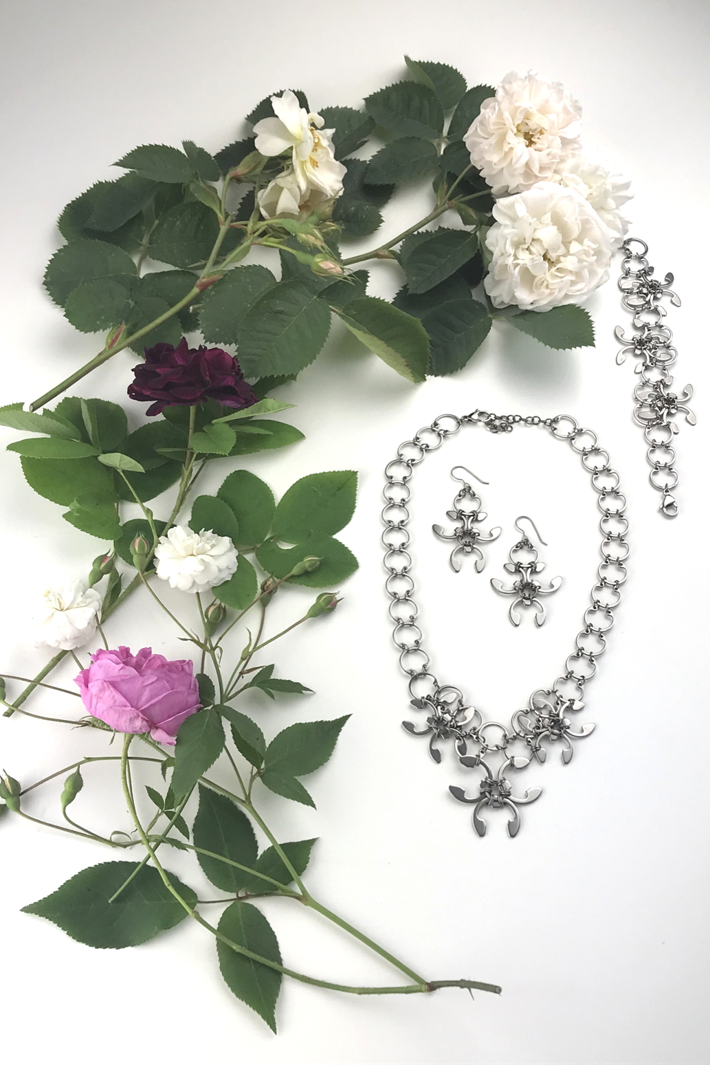 Flatlay of old roses (Rosa alba, Rosa gallica officinalis, moss rose 'Capitaine John Ingram', & 'Felicite et Perpetue') with the Garland Necklace, Garland Earrings, and Garland Bracelet in Wraptillion's studio.