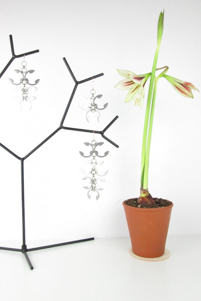 Desk photo from Wraptillion's studio with a black metal tree with Wraptillion's Bold Wisteria Ornament, Bold Trellis Ornament, Long Wisteria Ornament, and an opening flower and two more buds on light green and red striped amaryllis (hippeastrum) 'Dragonfly' (from the Sonatini collection), growing in a tall terracotta rose pot.