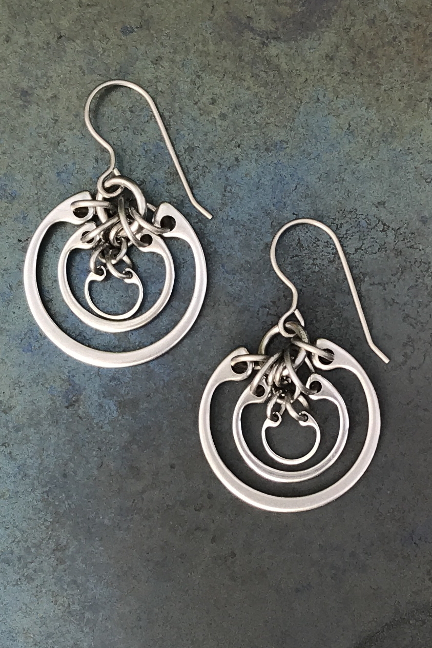 A pair of silver-colored dangle earrings with three concentric circles, on a mottled blue background.