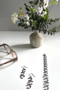 A small arrangement of late winter flowers on a white desk with reading glasses, earrings, and a bracelet.