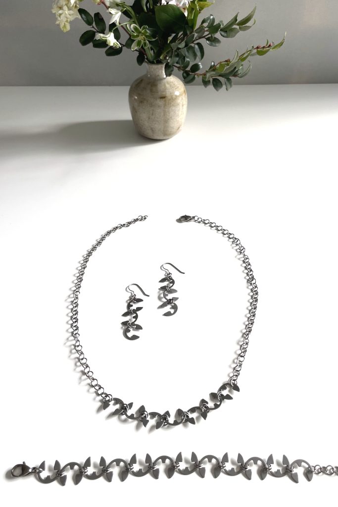 A small arrangement of late winter flowers on a white desk with earrings, a necklace, and a bracelet.